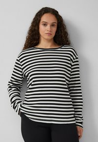 Schwarz-weißer, gestreifter, langärmeliger Baumwolloberteil mit Rundhalsausschnitt und gerippter Textur, kombiniert mit schwarzen Hosen.