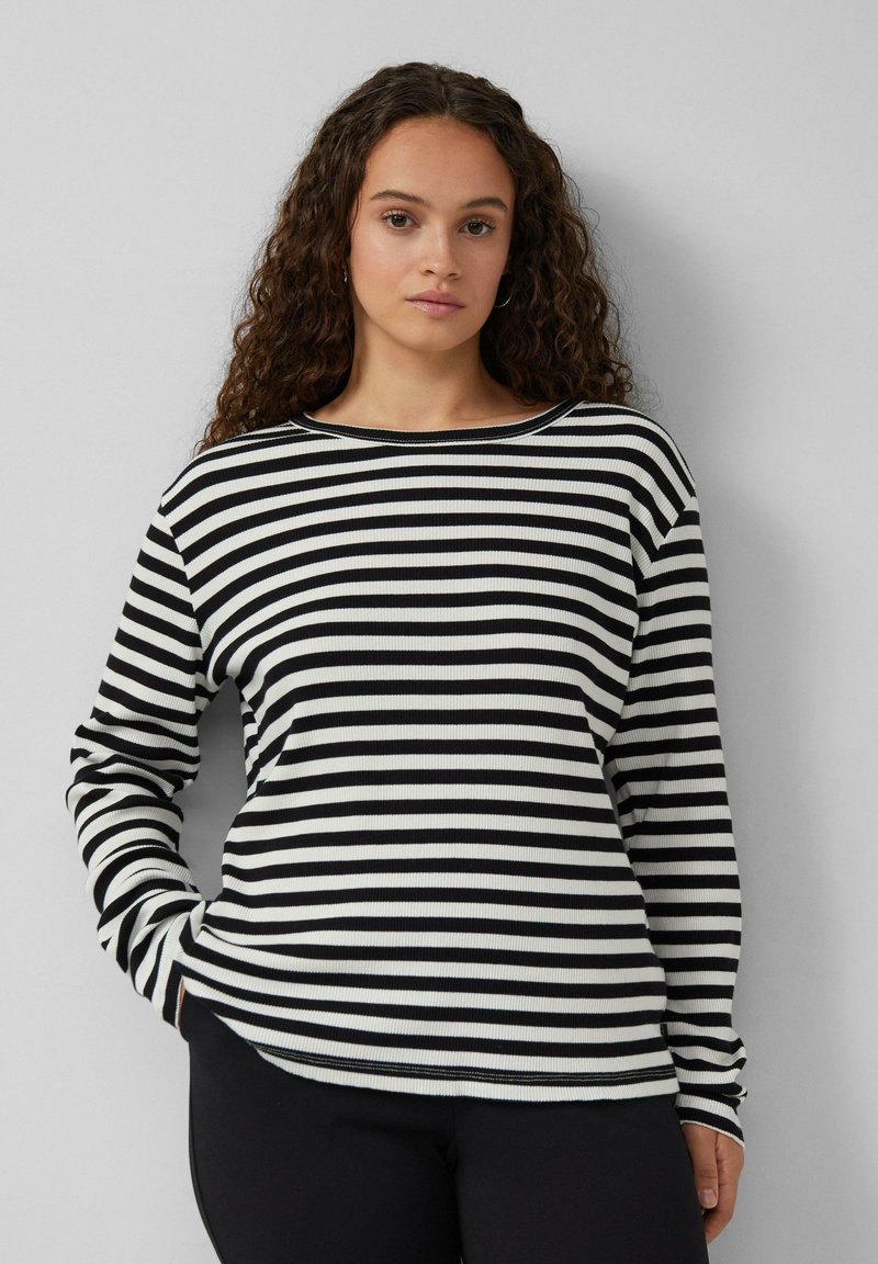 Schwarz-weißer, gestreifter, langärmeliger Baumwolloberteil mit Rundhalsausschnitt und gerippter Textur, kombiniert mit schwarzen Hosen.