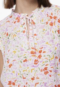 Kwiatowa bluzka z lekkiego, teksturowanego materiału. Posiada okrągły dekolt, detal w postaci wiązania oraz wyrazisty wzór w odcieniach pomarańczowym, różowym i zielonym.