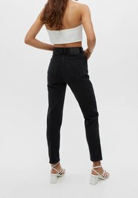 Jean noir taille haute avec une coupe droite, en denim, avec un ourlet légèrement usé. Porté avec des sandales blanches à talons et à brides.