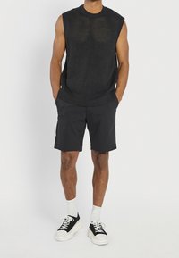 Top de punto negro texturizado sin mangas combinado con pantalones cortos negros, calcetines blancos y zapatillas negras con suelas blancas.