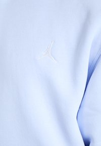 Šviesiai mėlynas džemperis su švelnia tekstūra, su balta siuvinėta Jumpman logotipo detalė priekyje. Paprastas dizainas su laisvu pritaikymu.
