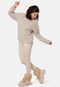 Strickpullover in Hellbeige mit mehrfarbigen Sprenkeln; eng anliegende cremefarbene Hose; braune, mit Fell gefütterte Stiefel mit dicken Sohlen und Schnürsenkeln.
