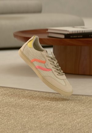 Beige sneaker med en tekstureret mesh-overdel, med pink og gule accenter, rund snude og beige gummisål. Snørebåndene er lysegrå.