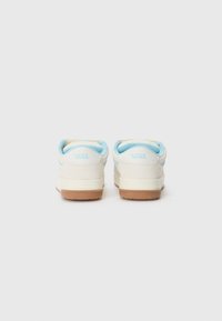 White canvas sneakers with light blue accents and gum rubber soles. Features a rounded toe and a padded collar for comfort.