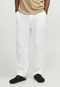 Białe lniane spodnie z bocznymi kieszeniami, luźny krój i prosty fason. Połączone z czarnymi butami wsuwanymi i beżową koszulką.