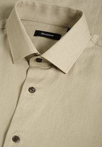 Ljust beige strukturerad skjorta med knapp ner-krage, prydd med mörkbruna knappar och en etikett broderad med "Matinique."