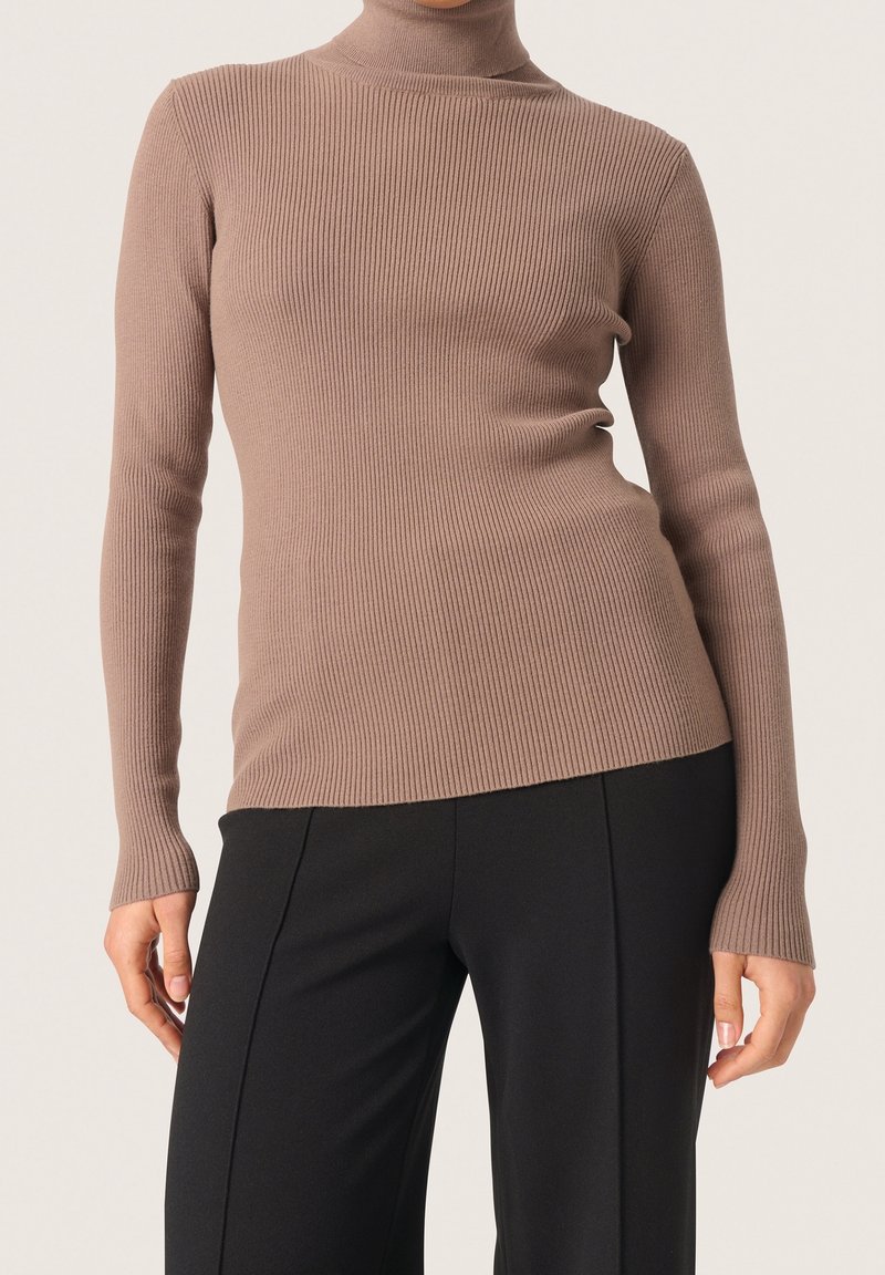 Maglione a collo alto a costine color marrone chiaro, caratterizzato da una silhouette aderente e maniche lunghe, abbinato a pantaloni neri a gamba larga.