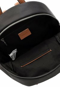 Black backpack open to show interior with zippered pocket, brown leather tag, fabric label, and an internal slot pocket with leather trim.