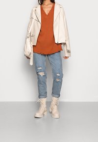 Vit läderjacka, bränd orange stickad topp med fransig fåll, ljusblå slitna jeans och beige snörstövlar.