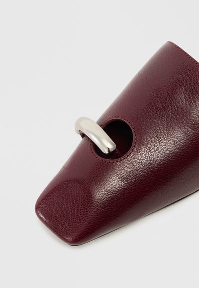 Burgundy leather shoe with a pointed toe, featuring a side cutout and metallic accent. Texture is pebbled, enhancing visual depth.