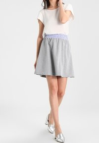 Falda de patinadora gris con una cinturilla de goma lavanda, combinada con una blusa blanca de manga corta; modelo lleva tacones plateados de punta. 