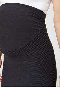 Jupe de maternité noire à côtes avec une taille haute, présentant des lignes verticales texturées et une finition lisse sur la partie inférieure.