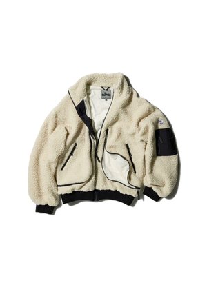 Cremefarvet faux fur-jakke med sorte detaljer, lynlåslukning foran, to sidelommer og elastiske manchetter. Patches detaljer på venstre ærme.