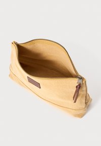Sacoche en toile jaune avec fermeture à glissière, dotée d'une patte en cuir, d'une texture lisse et d'un intérieur spacieux.