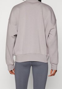 Sudadera gris de corte amplio, con hombros caídos y puños de canalé. Textura suave y diseño minimalista, combinada con mallas gris a juego.
