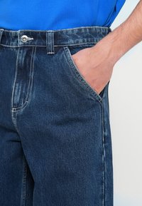 Χέρι που ακουμπά μέσα στην μπροστινή τσέπη ενός μπλε τζιν τζιν ωραίο με φωτεινό μπλε πουκάμισο.