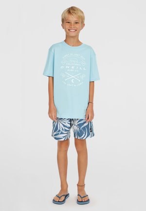 Svijetloplavi pamučni majica sa bijelim grafičkim printom. Tamnoplave kratke hlače s bijelim uzorkom lista. Akvamarin japanke. Casual plažni outfit.