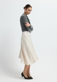 Grijze lange mouw top, crèmekleurige flared midi-rok en zwarte schoenen met een lage hak. Gladde textuur, op maat gemaakt ontwerp en gestructureerde silhoeet.