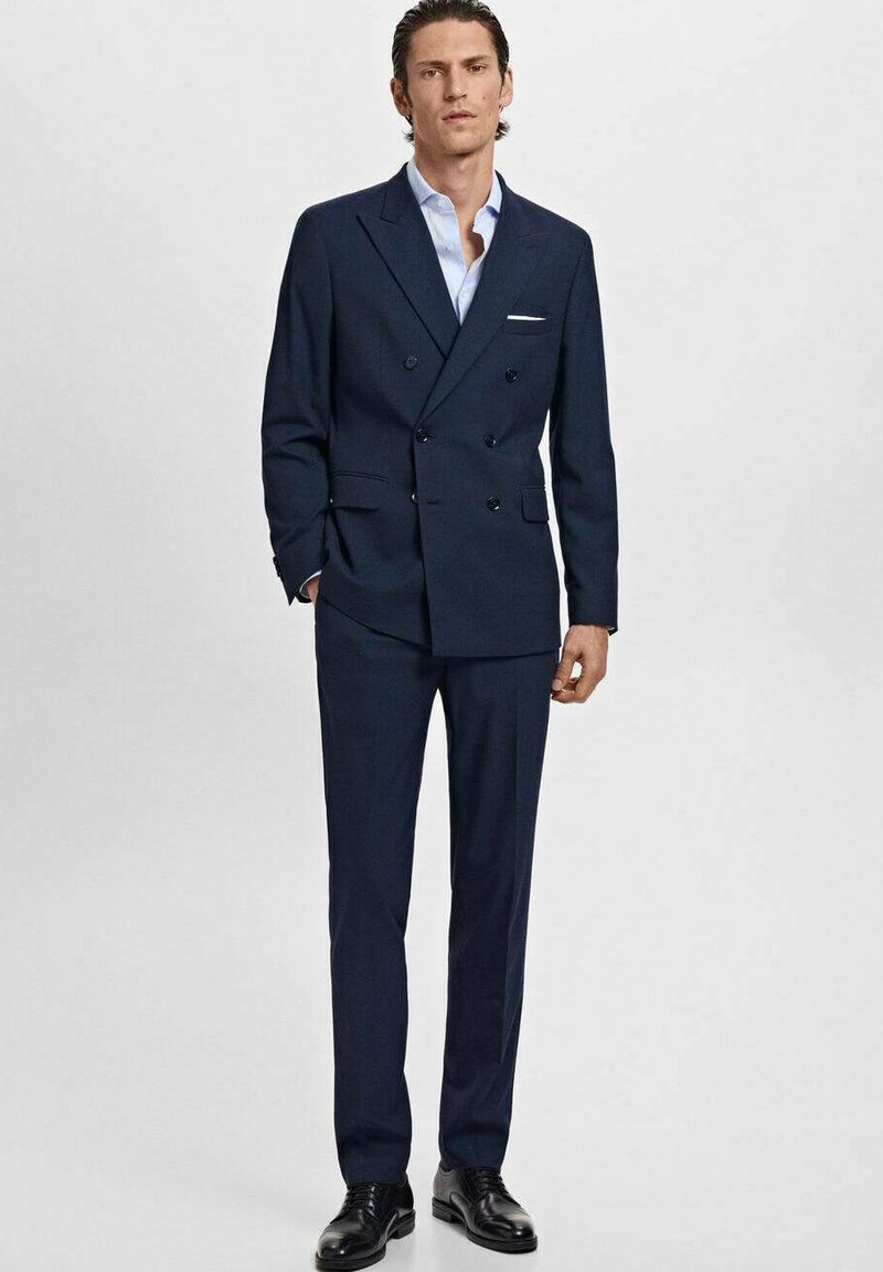 Marineblaues, doppelt geknöpftes Anzugjackett mit glatter Textur, passende Hose und ein hellblaues Hemd, ergänzt durch schwarze Lederschuhe.