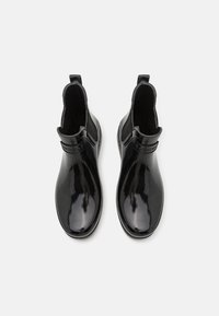 Mustad mustad ankle boots, mis on valmistatud kummist ja millel on sile tekstuur, elastsete külgpaneelide ja väikese tõmmetaasiga, et neid oleks lihtne jalga panna.