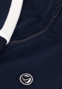 Dunkelblaues Sweatshirt mit einem weißen Reißverschluss, ausgestattet mit einem runden Logo-Patch und strukturiertem Stoff. Enthält eine kontrastierende weiße Kordel.