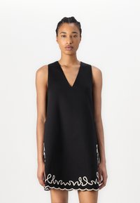 Black sleeveless dress with a V-neck, featuring white scalloped embroidery at the hem. Smooth fabric, relaxed fit, knee-length.