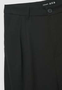 Pantaloni neri con una texture liscia, chiusura con un singolo bottone e tasche frontali. L'etichetta indica le taglie in più standard.