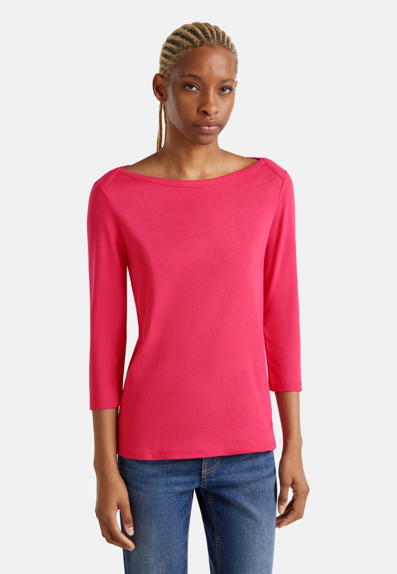 Fuchsia Hemd mit drei Viertelärmeln aus weichem Stoff, mit einem Bootsausschnitt und einer taillierten Silhouette. Kombiniert mit Jeans.