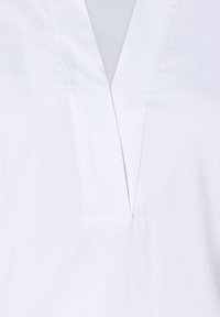 White cotton blouse with a V-neckline, featuring a simple design and visible stitching along the neckline.
