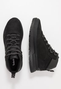 Bottes montantes en suède noir et synthétique avec des lacets noirs, semelle en caoutchouc texturée et œillets renforcés. Comprend une languette au talon.