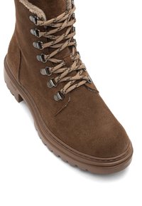 Botte d'hiver en daim marron avec doublure en fourrure, œillets en métal, lacets motif et semelle en caoutchouc épaisse, conçue pour une utilisation en extérieur par temps froid.