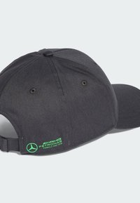 Svart keps med böjd skärm, tillverkad av tyg. Har en grön AMG Petronas-logga och ett justerbart band bak. Två ventilationshål.