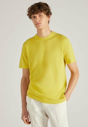 Geel T-shirt met korte mouwen en een ronde hals, met een gladde textuur en een comfortabele pasvorm. Gecombineerd met lichtgekleurde broeken.