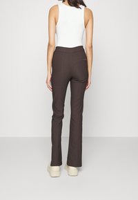 Bruna skräddarsydda byxor i ett glatt tyg, med en figursydd midja och raka ben. Bärs med en enkel vit topp och beige skor.