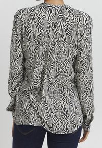 Camicetta a righe zebrate bianco e nero con maniche lunghe, dettaglio plissettato sul retro e polsini con bottone, realizzata in tessuto leggero.
