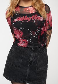 Black mesh top with red and white splatter pattern, featuring "Motley Crue" graphic in the center, paired with a black denim skirt.