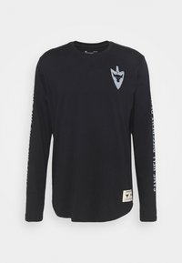 Czarna koszula z długim rękawem z bawełny, z jasnoniebieskim logo tarczy na piersi i napisem wzdłuż lewego rękawa. Metka na dole.