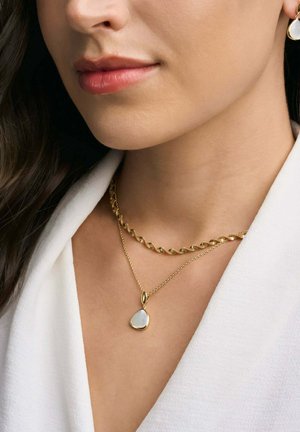 Collana a catena dorata attorcigliata sovrapposta a una delicata catena dorata con un pendente a forma di goccia con una pietra bianca. Colletto in morbido tessuto.