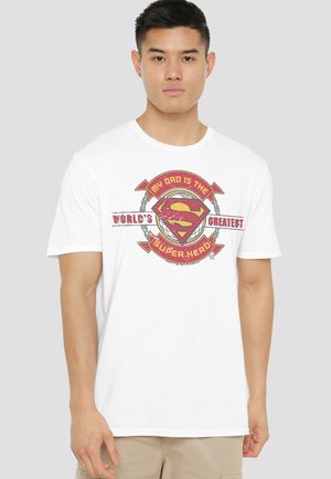Young man wearing a white t-shirt with a red and yellow Superman logo and the text "My dad is the world's greatest superhero."