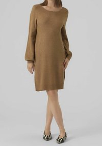 Robe en tricot marron à manches longues avec un col rond, texture douce et fentes sur les côtés. Associée à des ballerines à motif zèbre noir et blanc.