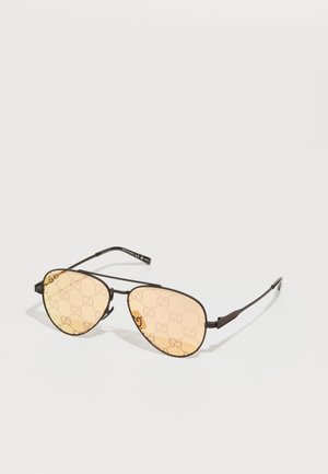 Óculos de sol com uma armação metálica escura e fina e lentes de tom âmbar com um padrão de logótipo repetido. Design leve com hastes curvadas.