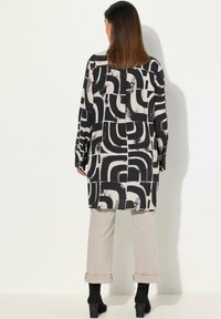 Langemouwblouse met een zwart-wit geometrisch patroon, met een rechte snit en een ontspannen pasvorm, gecombineerd met lichtgekleurde broeken en enkellaarsjes.
