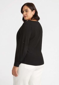Blusa nera a maniche lunghe con scollatura rotonda, caratterizzata da maniche arricciate e dettagli con bottoni, abbinata a pantaloni bianchi. Tessuto liscio.