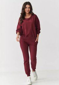 Burgundowy zestaw bluz i spodni dresowych wykonany z miękkiej tkaniny. Luźny krój z ściągaczami przy mankietach i w pasie. W połączeniu z białymi sneakersami.
