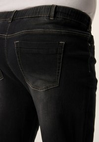 Mustat farkut, joissa on slim fit -leikkaus, takataskut, huomaamattomat ompelut yksityiskohdat ja hieman haalistunut pinta. Vyötärönauha on joustava.