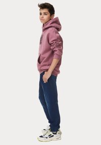 Sudadera con capucha rosa y bolsillo frontal, combinada con pantalones jogger azules. Zapatillas blancas y negras con acentos neón.