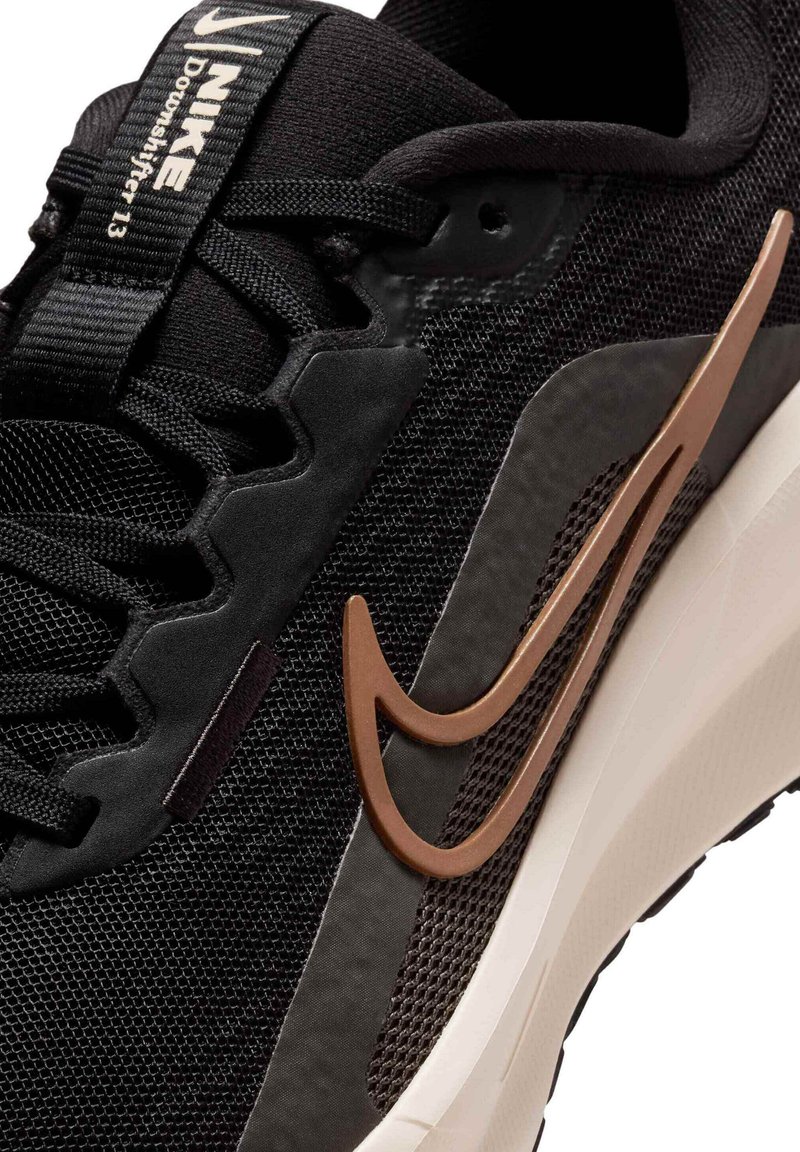 Zwarte synthetische sportschoen met een bovenwerk van mesh, een contrasterend bronzen Nike-logo en een witte middenzool. Voorzien van gestructureerde overlays en een vetersluiting.