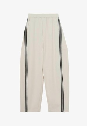 Világos bézs nadrág laza szabással, két oldalzsebbel és fekete függőleges csíkokkal a külső varrások mentén. Puha anyag, rugalmas derékrésszel.