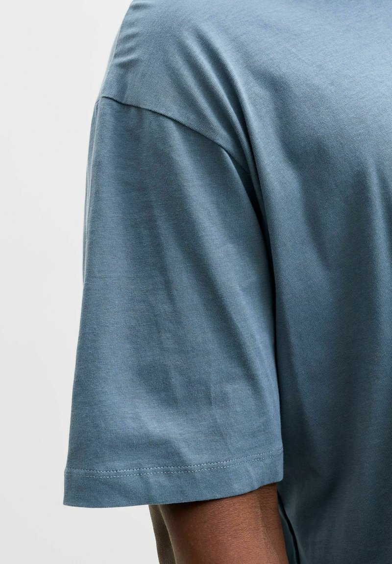 Camiseta de manga corta azul claro hecha de algodón suave. Presenta un cuello redondo y una textura lisa con un acabado simple y limpio.